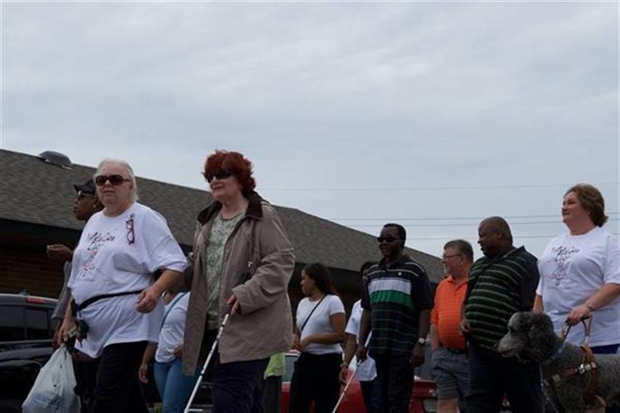 A group of consumers using white canes walk together at White Cane Day.